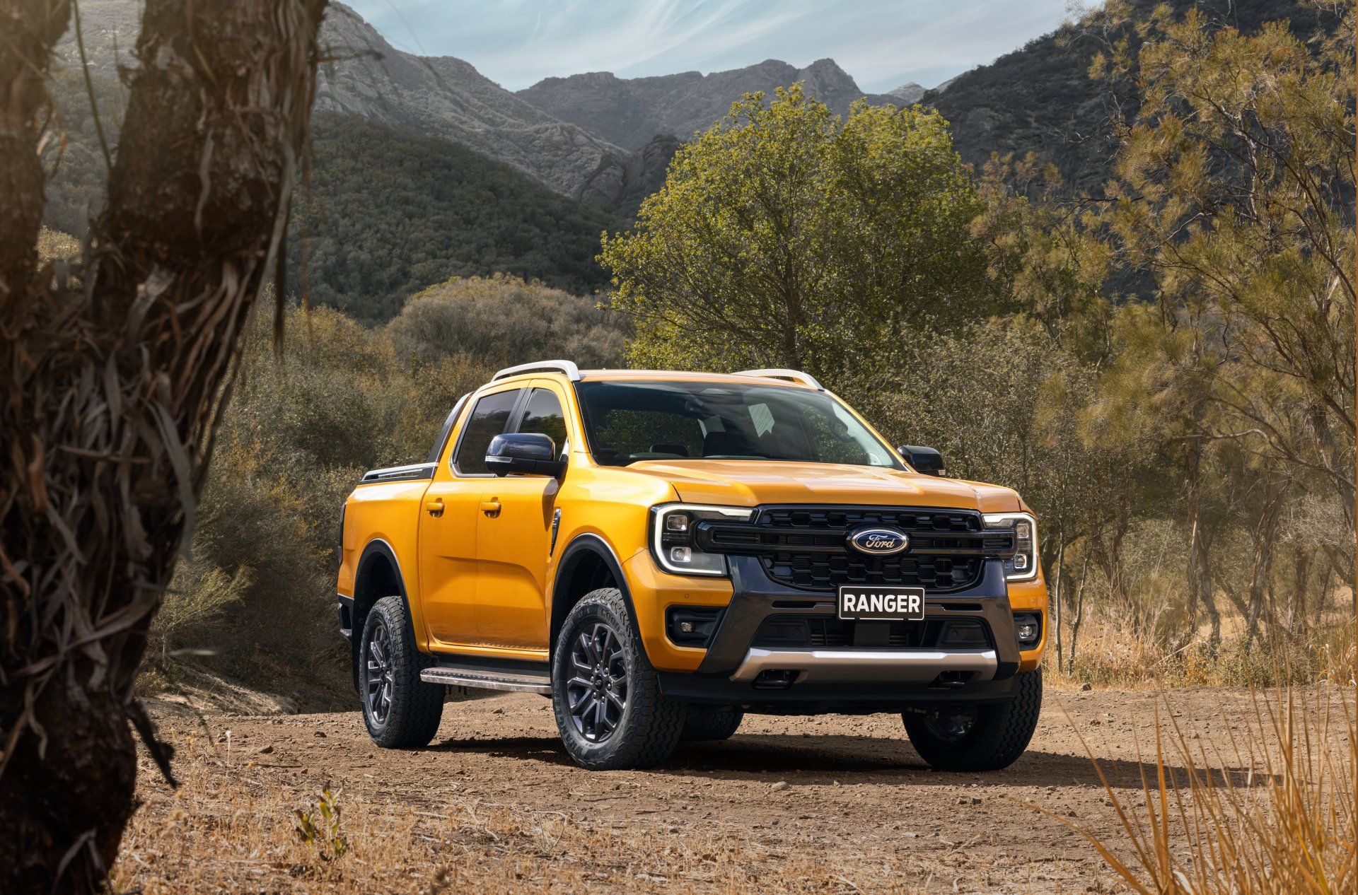 Yellow Ford Ranger pickup truck on a dirt road in a desert landscape.