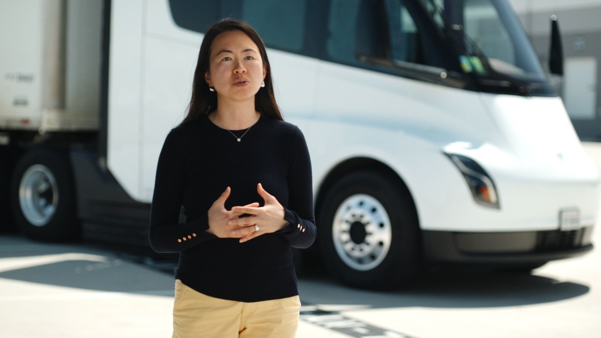 Woman standing in front of a white semi-truck; outdoors, day.