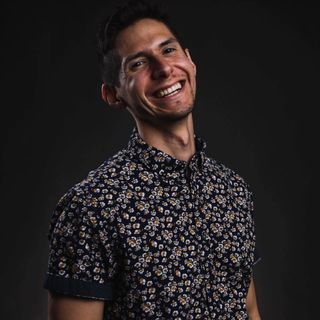 Man smiling broadly, wearing a floral shirt, against a dark gray background.