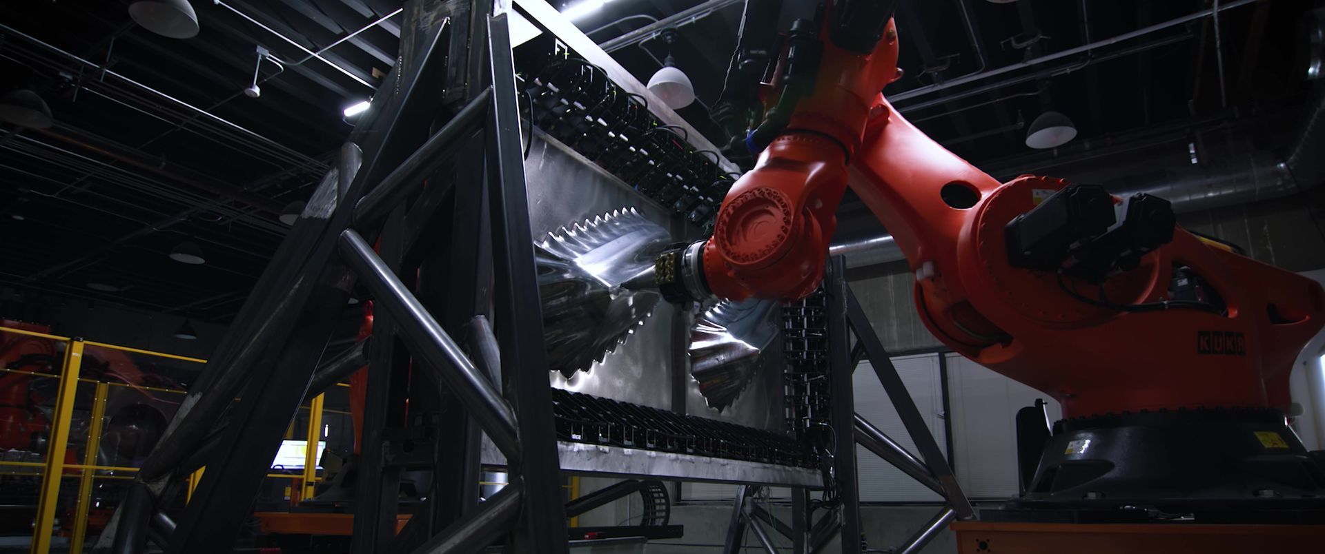 An industrial robot arm working on a large metal structure in a factory setting.