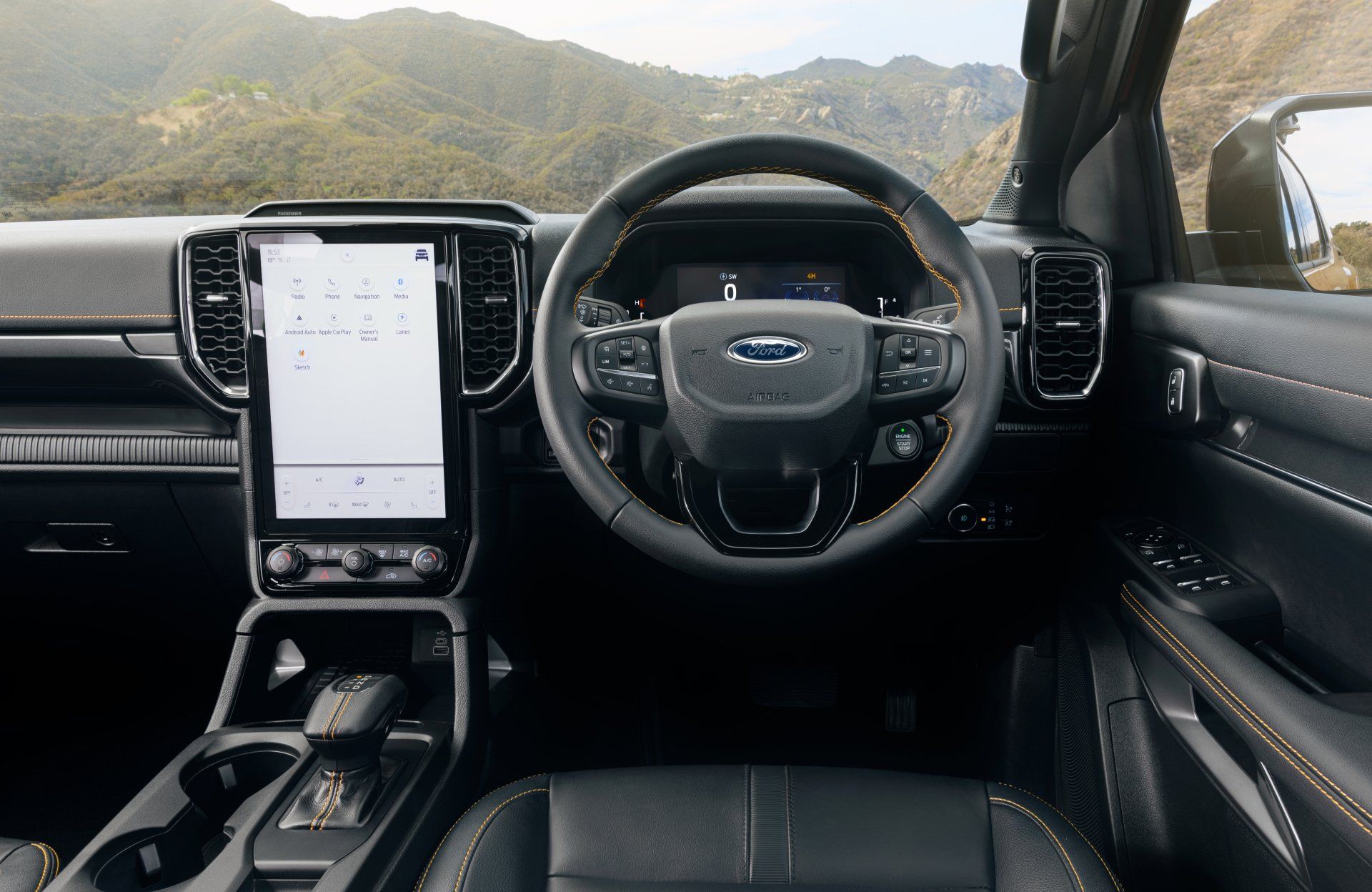 Interior view of a black Ford Ranger dashboard with a large touchscreen, steering wheel, and mountain backdrop.