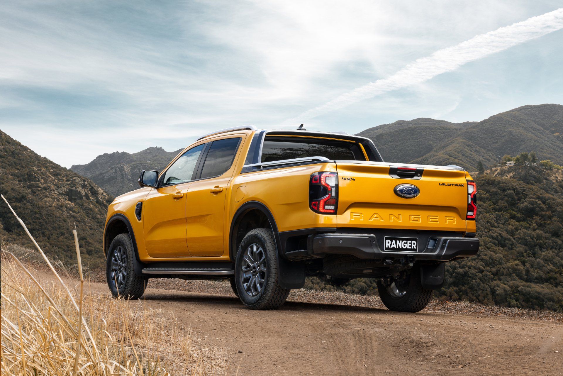 Yellow Ford Ranger truck on a dirt road, mountains in the background.