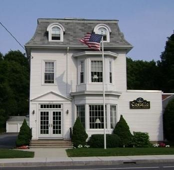 White building with US flag, possibly a funeral home, with arched windows and a mansard roof.