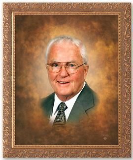Portrait of a smiling older man in a suit and glasses, within a decorative gold frame.