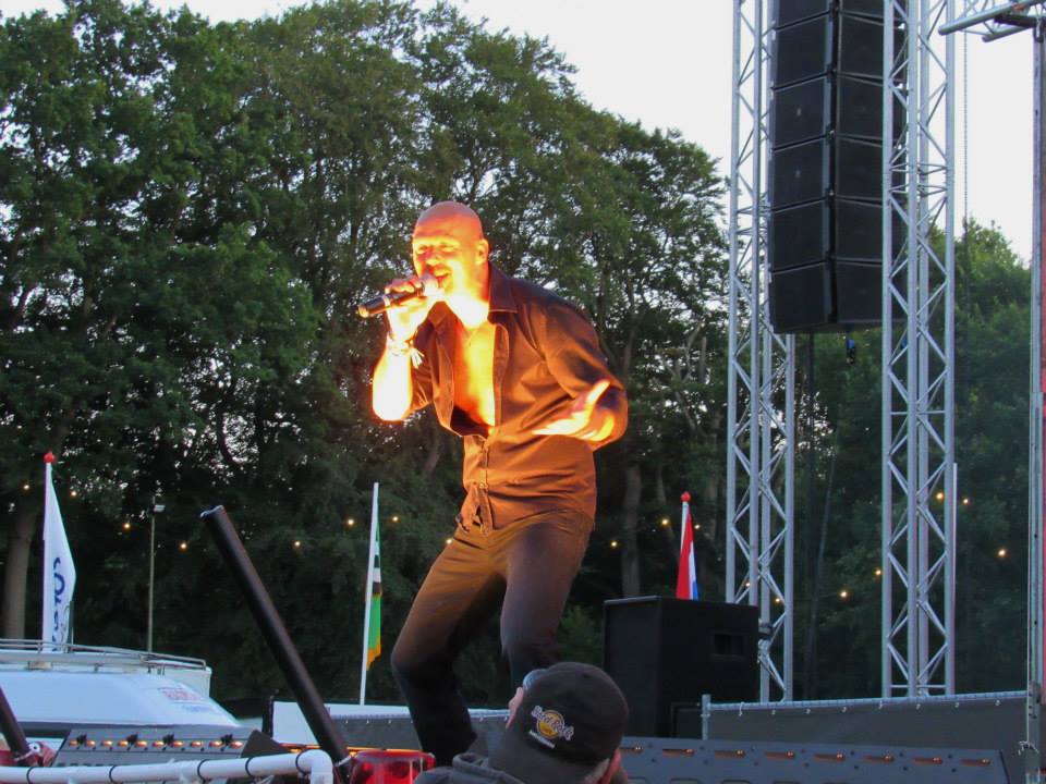 Zangeres treedt op op een openluchtpodium bij zonsondergang, verlicht door fel oranje podiumlicht.