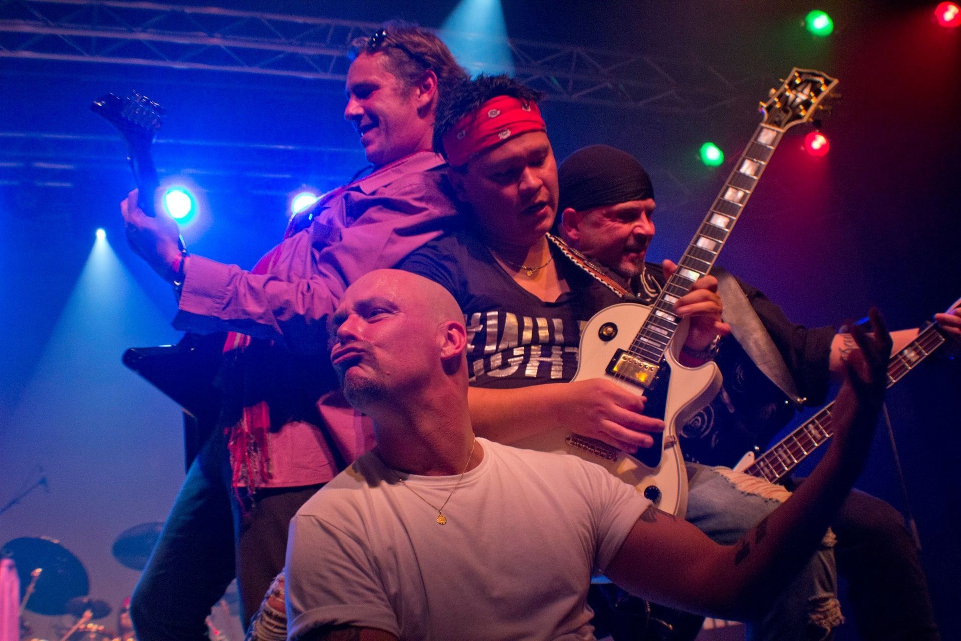 Vier muzikanten staan ​​op het podium onder blauwe en rode lichten; een van hen zingt in een microfoon en een ander speelt gitaar.