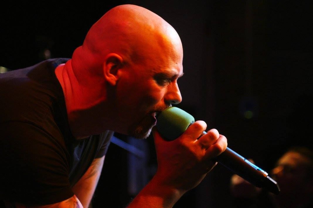 Zangeres zingt vol passie in een microfoon onder rode podiumverlichting.
