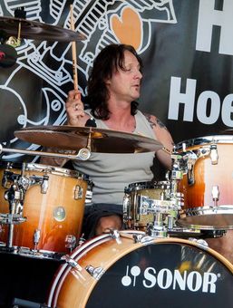Een drummer bespeelt een oranje Sonor-drumstel op het podium, met bekkens en een donkere achtergrond.