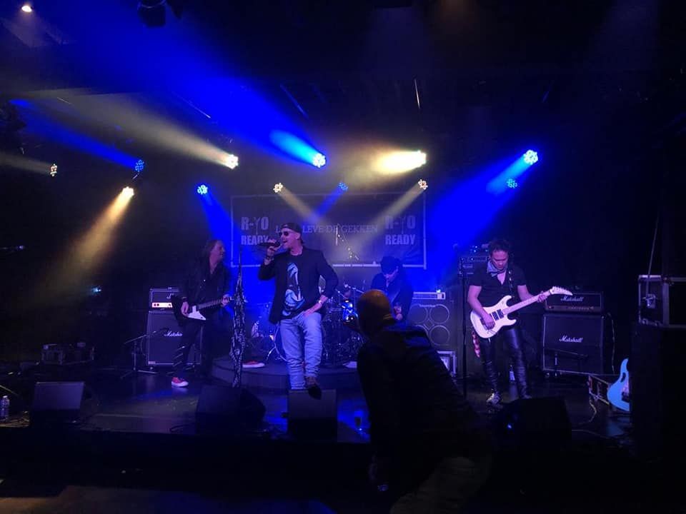 Liveband treedt op op een schemerig podium met blauwe spotlights en zichtbare instrumenten.