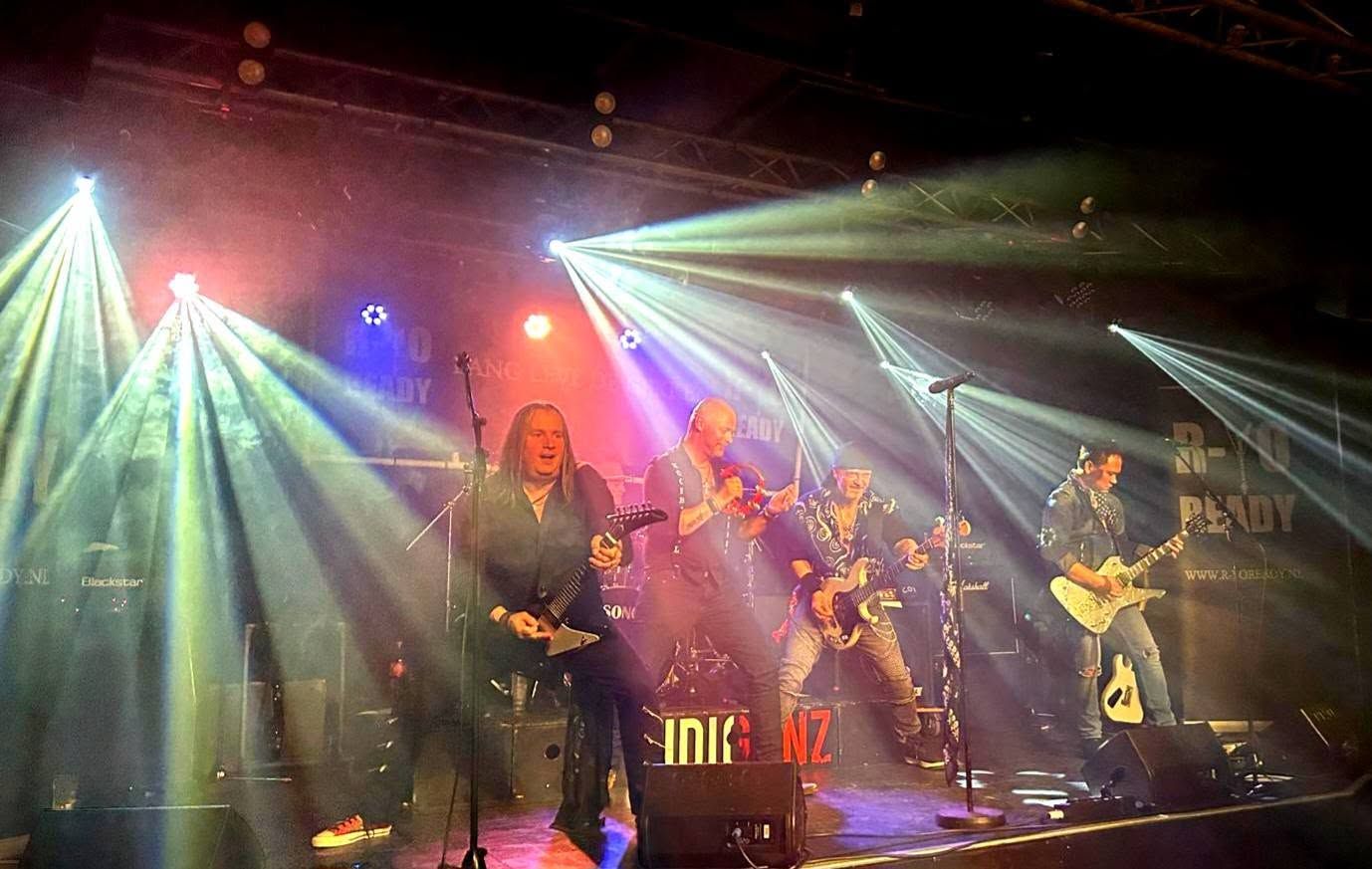 Band treedt op op een podium met felgekleurde lichten en rook.