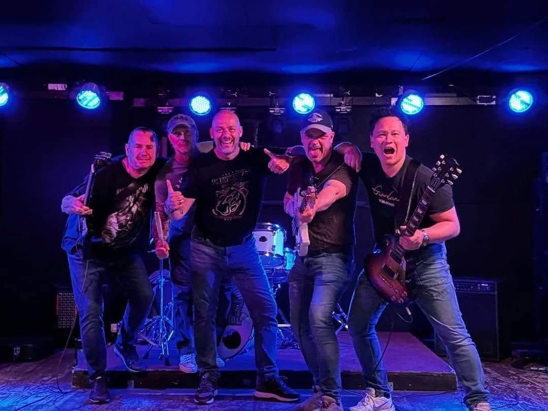 Vier muzikanten treden op een podium op onder blauw licht, zingend en gitaar en drums spelend.