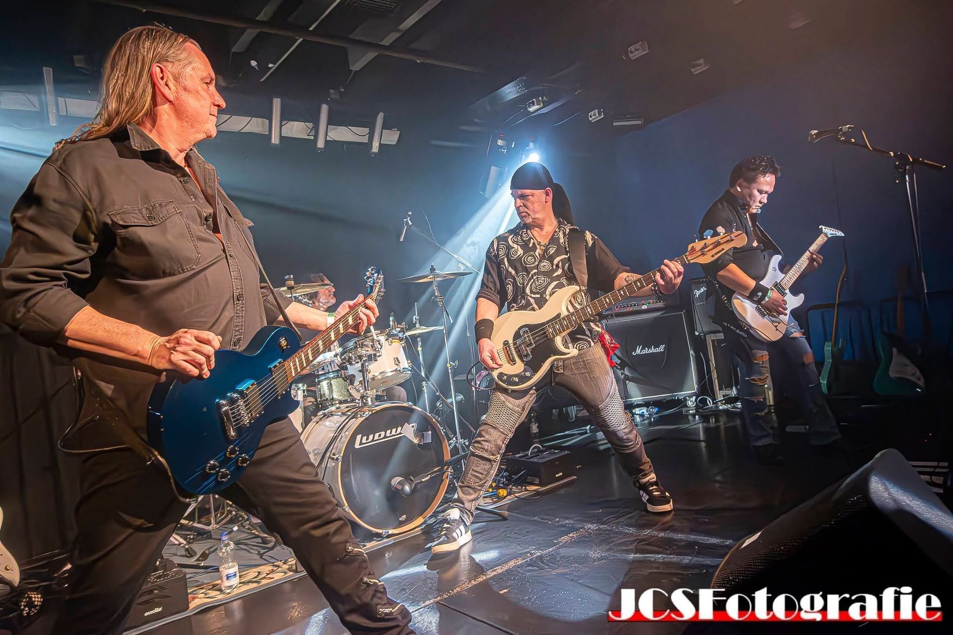 Rockband die live optreedt op een rokerig podium met elektrische gitaren en felle concertverlichting.