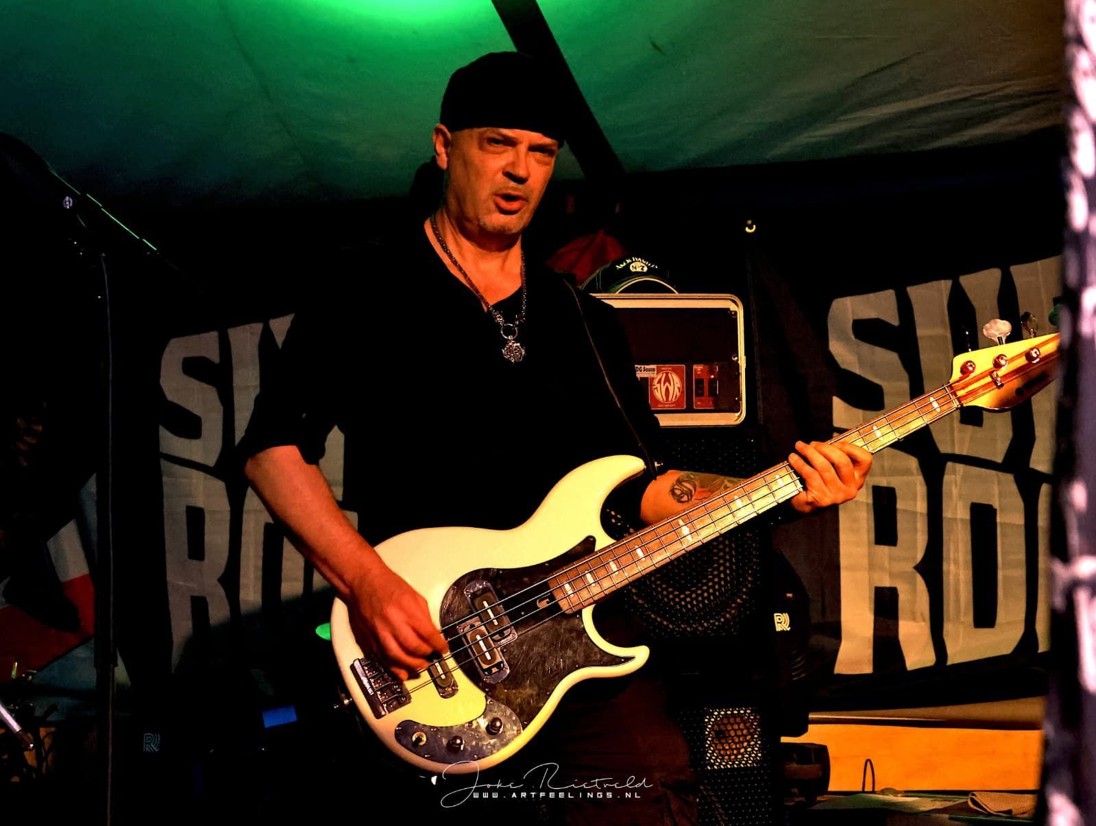 Muzikant die op een witte basgitaar speelt op het podium onder groene en rode lichten.