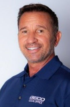 Portrait of a smiling man in a blue GEICO polo shirt on a light background