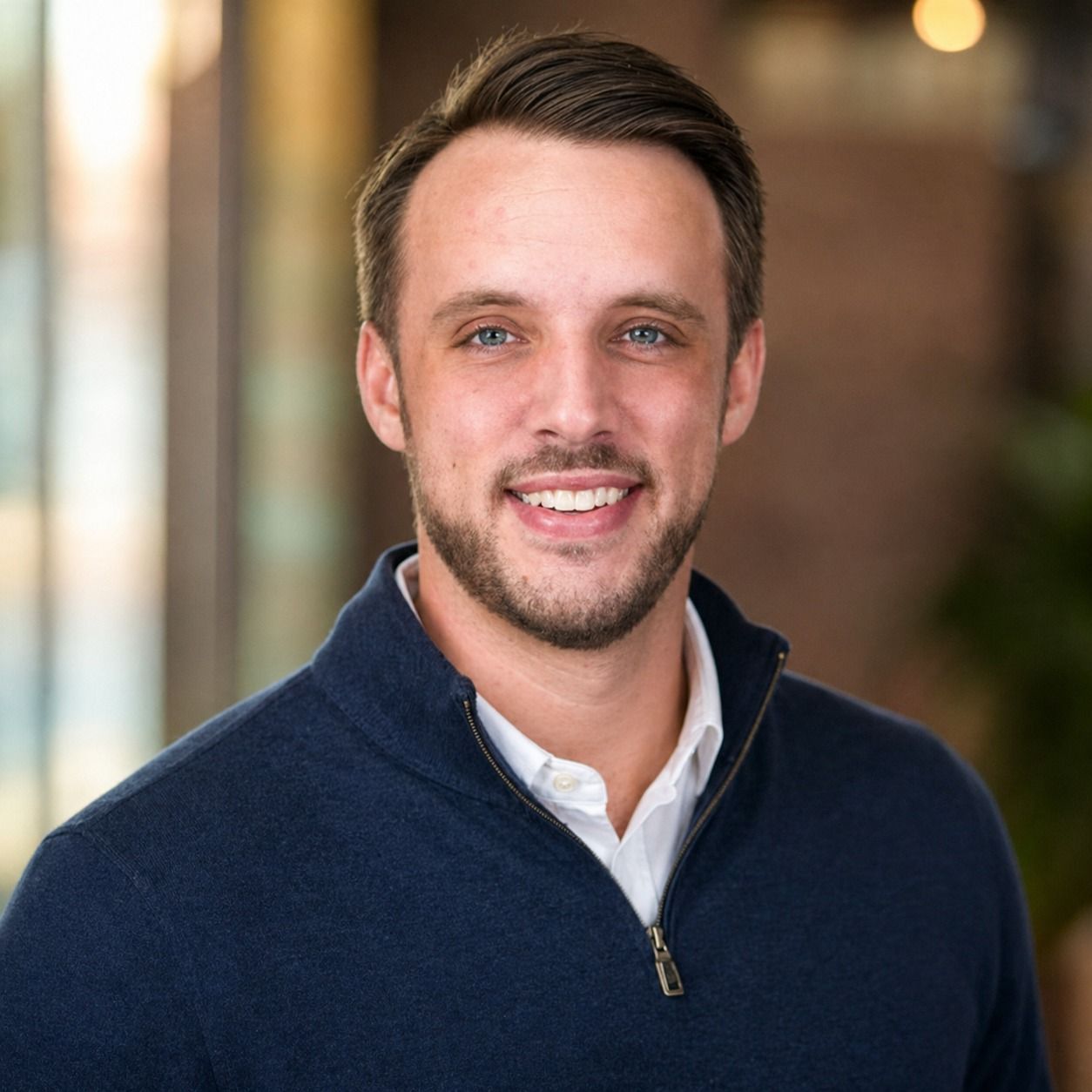 Smiling man in a navy quarter-zip sweater against a softly blurred indoor background