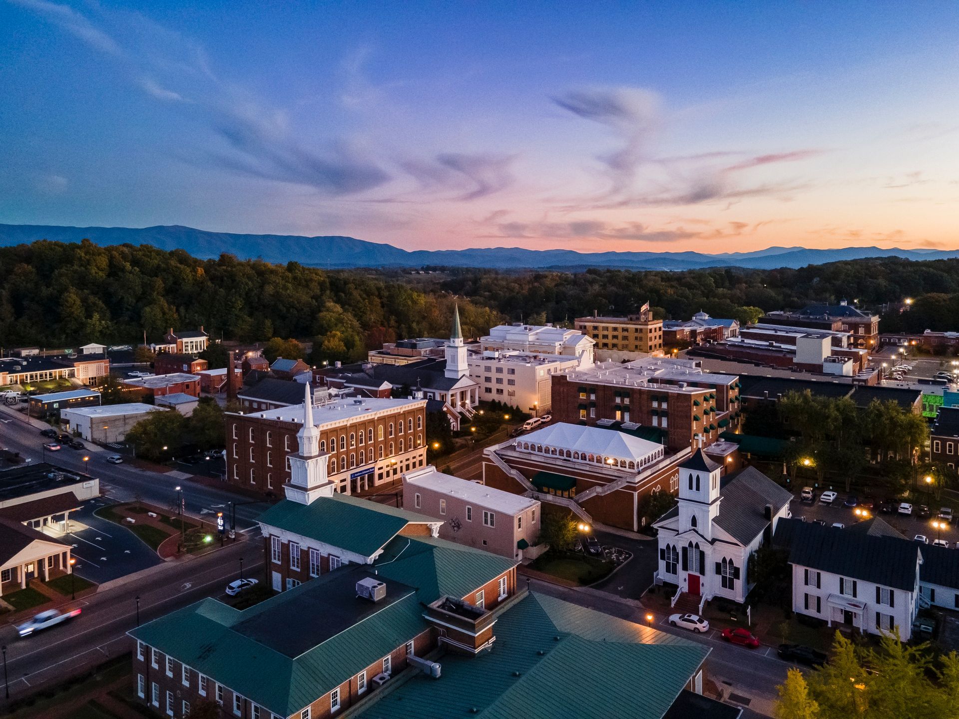 Downtown buildings at dusk with a sunset sky and distant hills behind the town