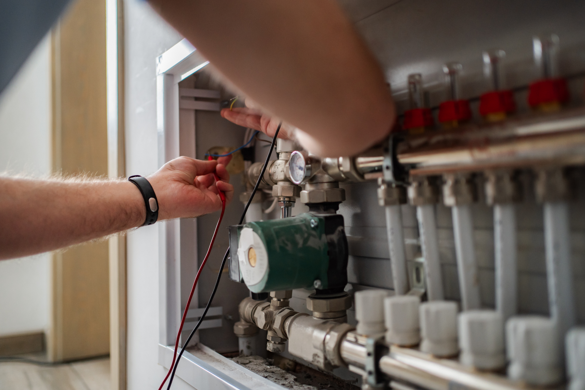 Technician adjusting valves on a heating manifold inside a utility cabinet