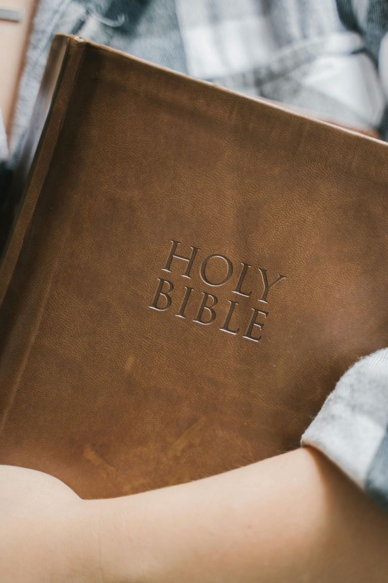 Contact Us Brown Holy Bible held against a plaid shirt sleeve
