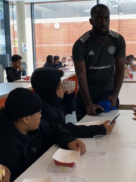 A man in a manchester united jersey is talking to a group of children