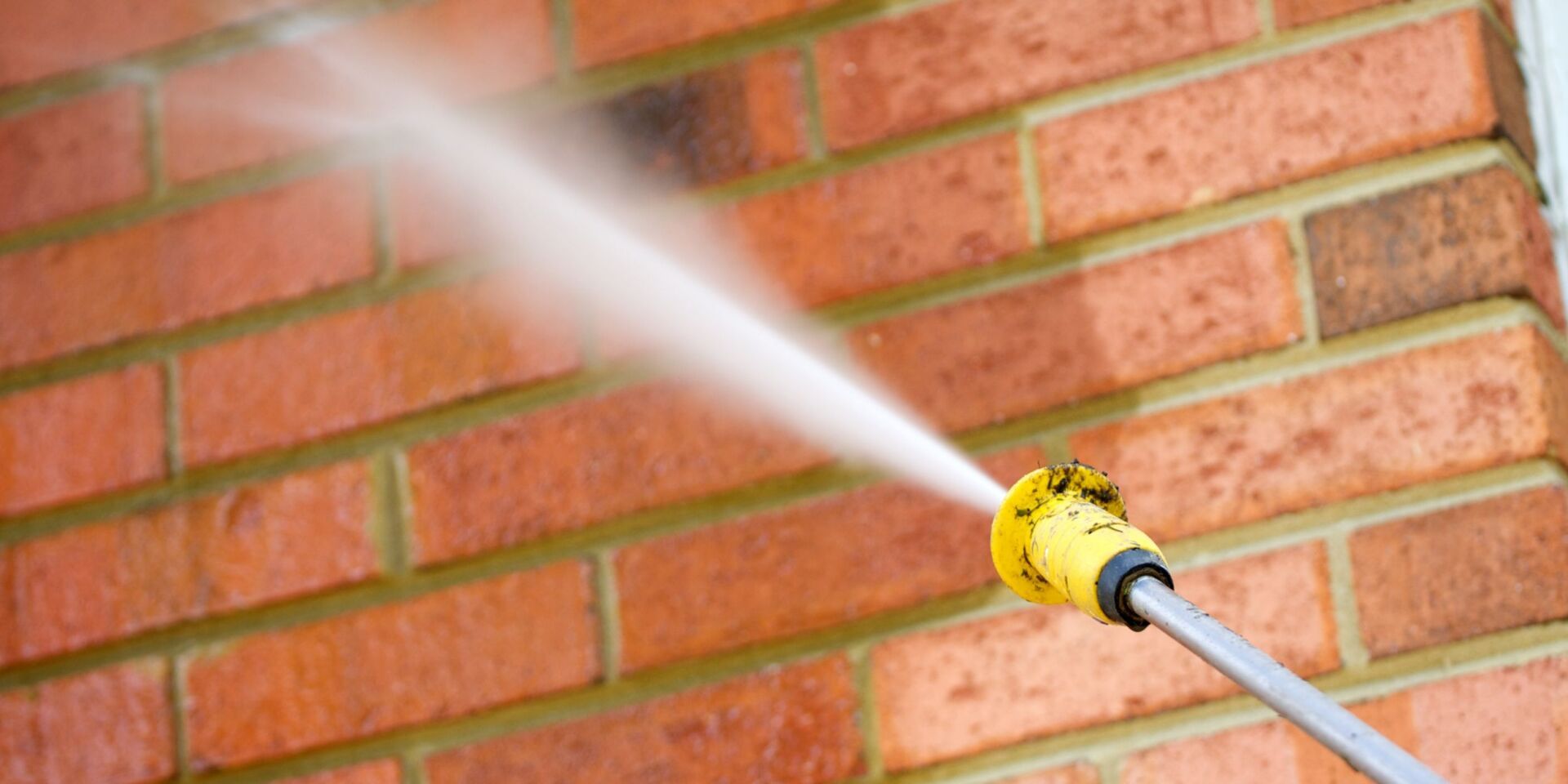 A pressure washer spraying water onto a red brick wall.