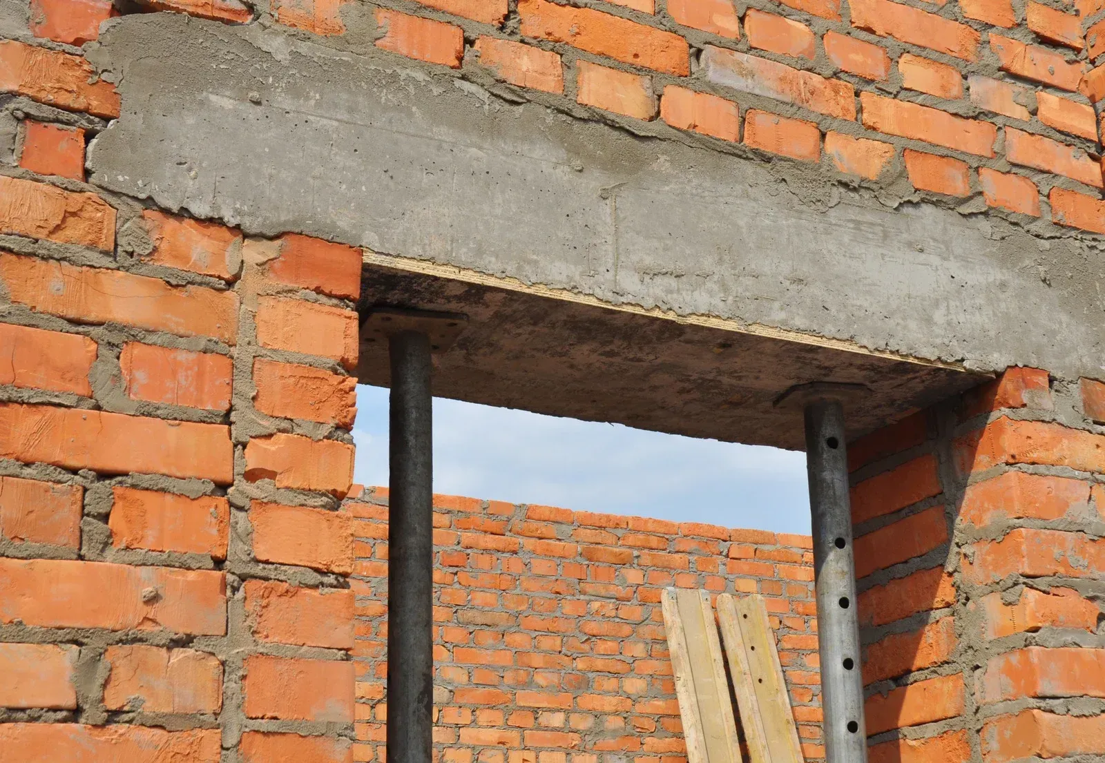 Brick wall with a concrete lintel over an opening; supported by metal jacks.