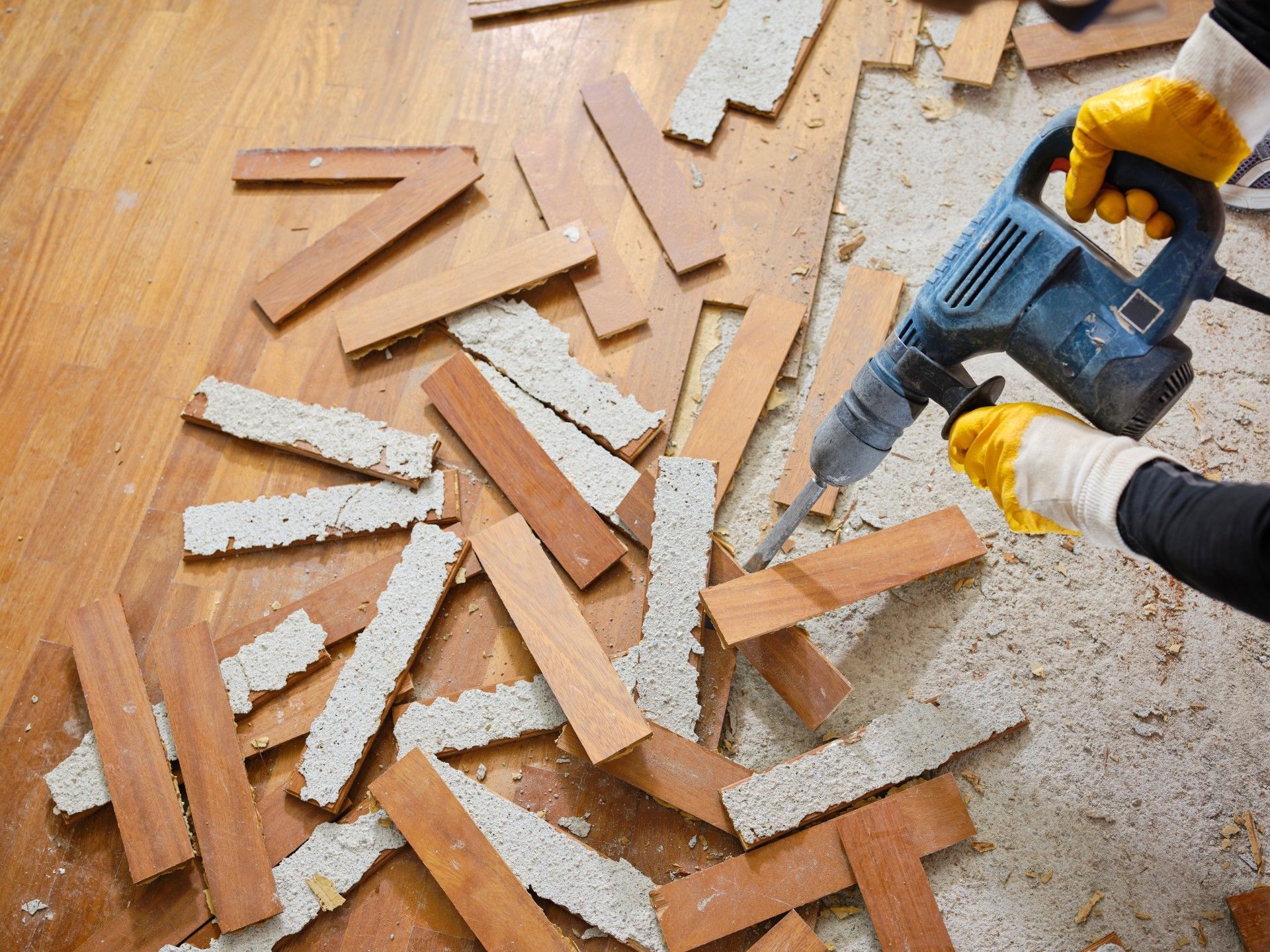 A person is using a hammer drill on a wooden floor.