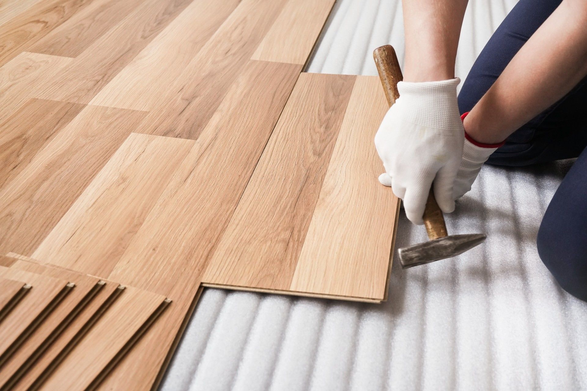 A person is installing a wooden floor with a hammer.
