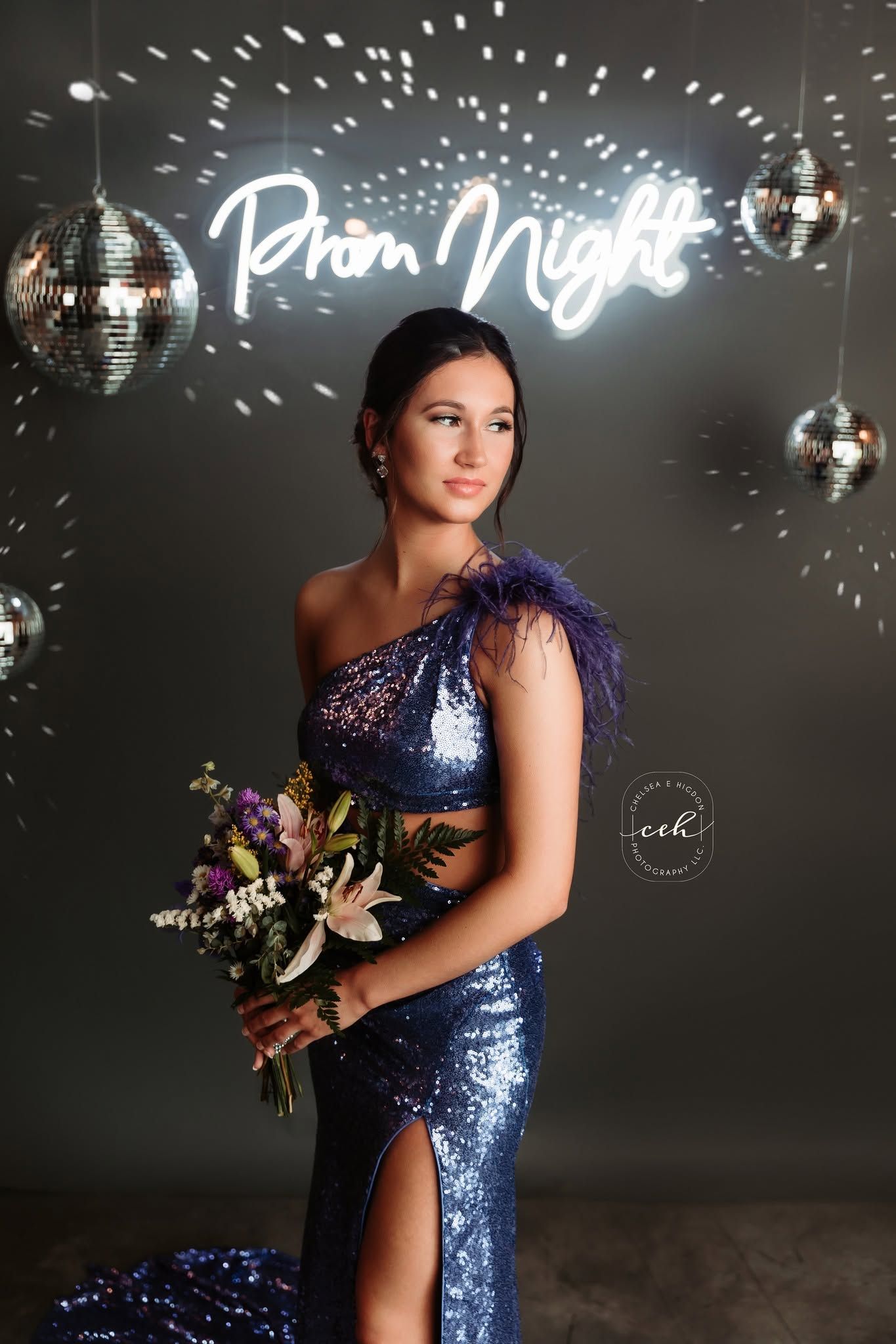 Prom night portrait of a person in a blue sequined gown holding a bouquet under neon signage and disco balls