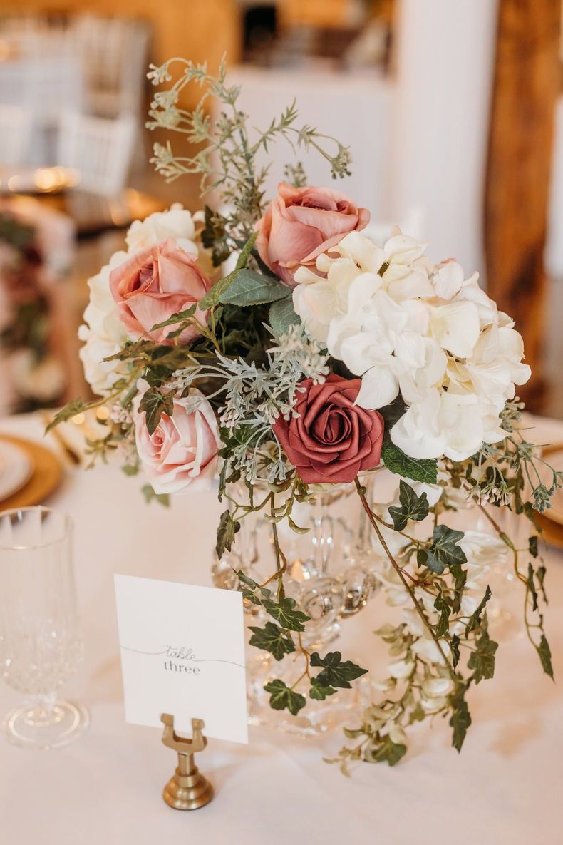 Pink and white floral centerpiece on a wedding reception table with greenery and candles