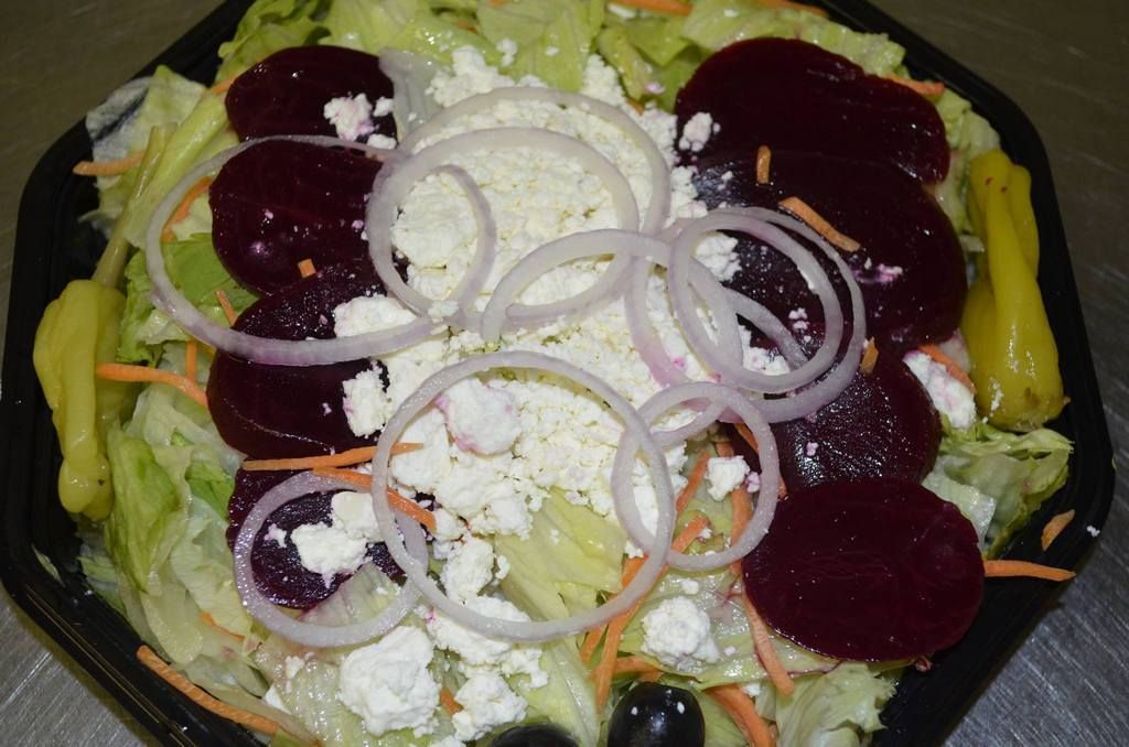 Salad with beets, feta, onions, carrots, lettuce, and pepperoncini in a black bowl.