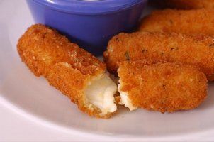 Fried mozzarella sticks, one broken open with melted cheese, on a plate with blue dipping sauce.
