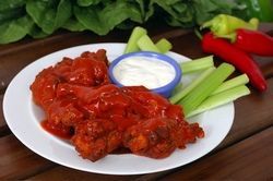 Plate of buffalo wings covered in red sauce, with blue cheese dip and celery sticks.