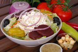 Salad bowl with lettuce, tomatoes, red onion, olives, feta, beets, pepperoncini, croutons, and dressing.