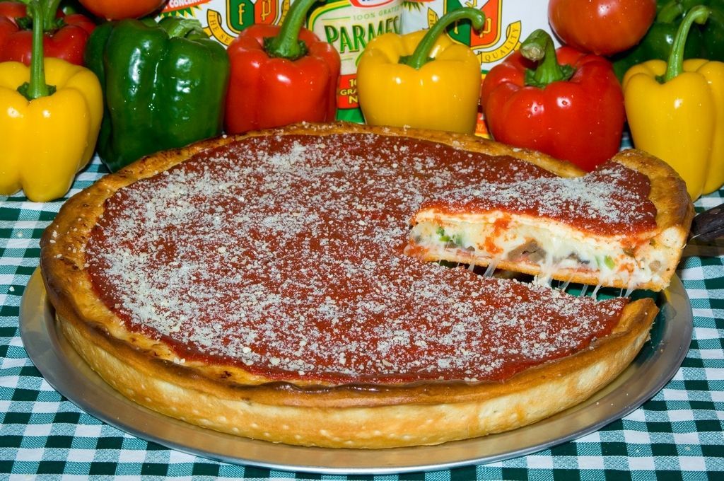 Deep-dish pizza with a slice removed, topped with sauce and cheese, surrounded by bell peppers.