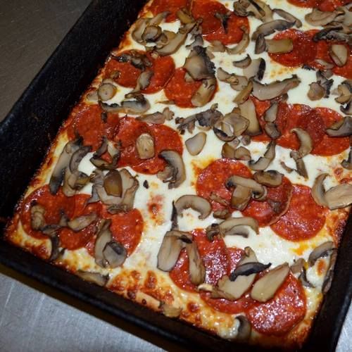 Square pizza with pepperoni and mushrooms in a black pan.