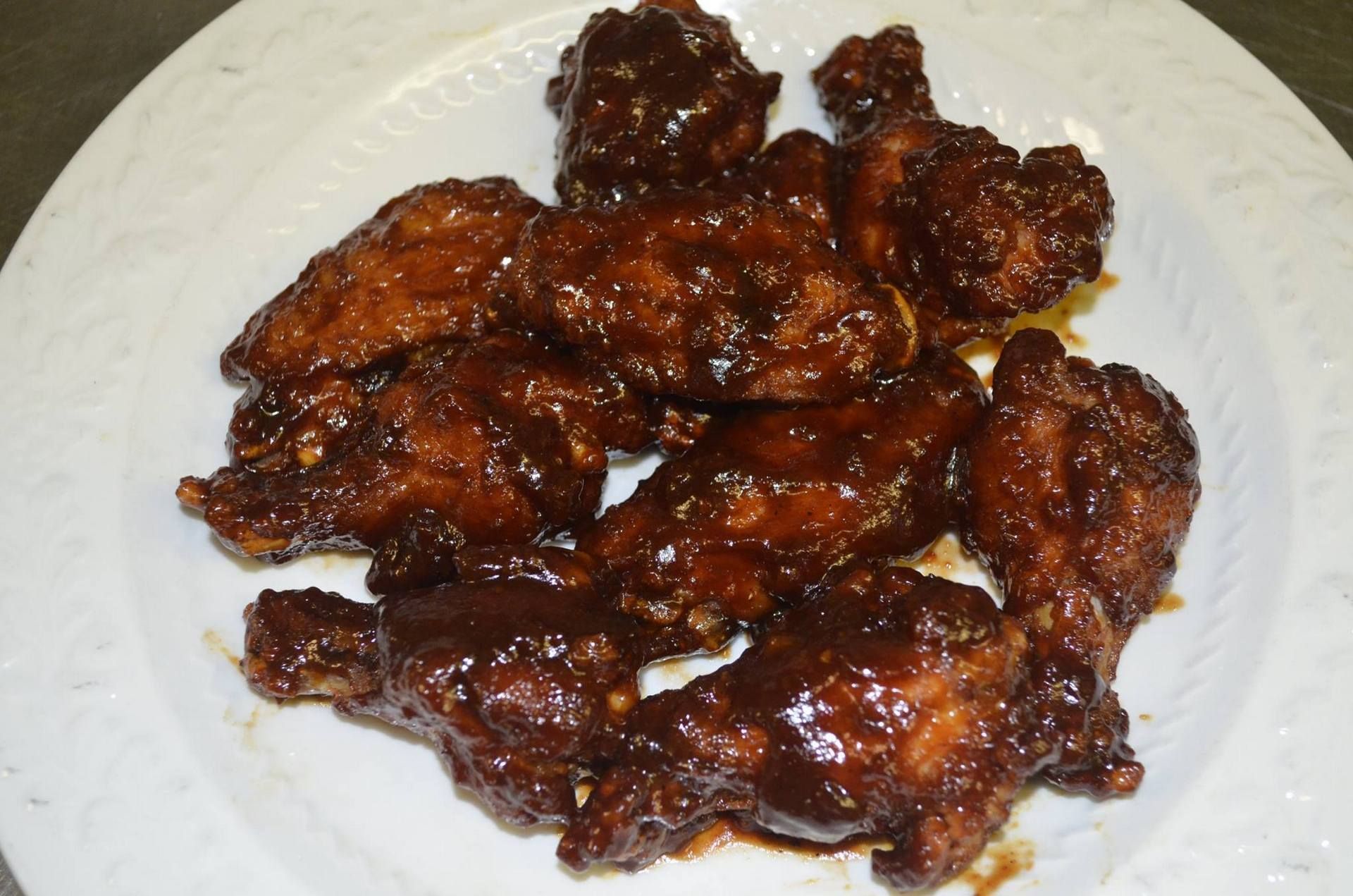 Plate of glazed chicken wings. Dark brown sauce covers the fried chicken pieces on a white plate.
