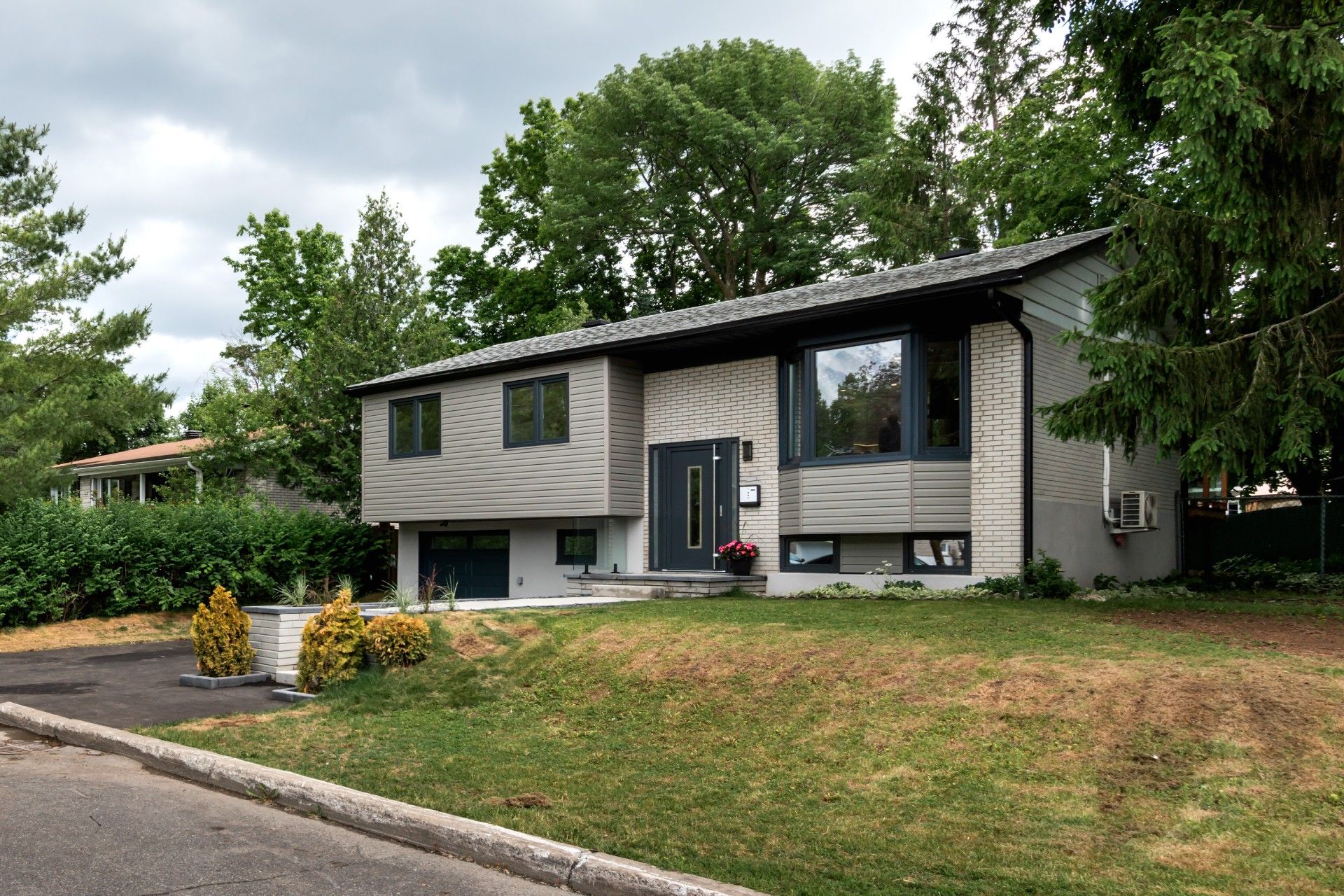 A tan, one-story house with a white porch, matching garage, and a large paved driveway under a clear blue sky.