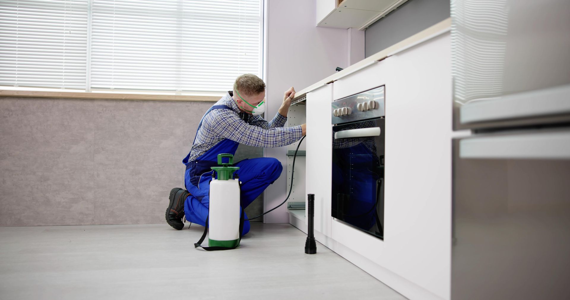 Person kneeling and cleaning a kitchen cabinet with a spray bottle and cloth.