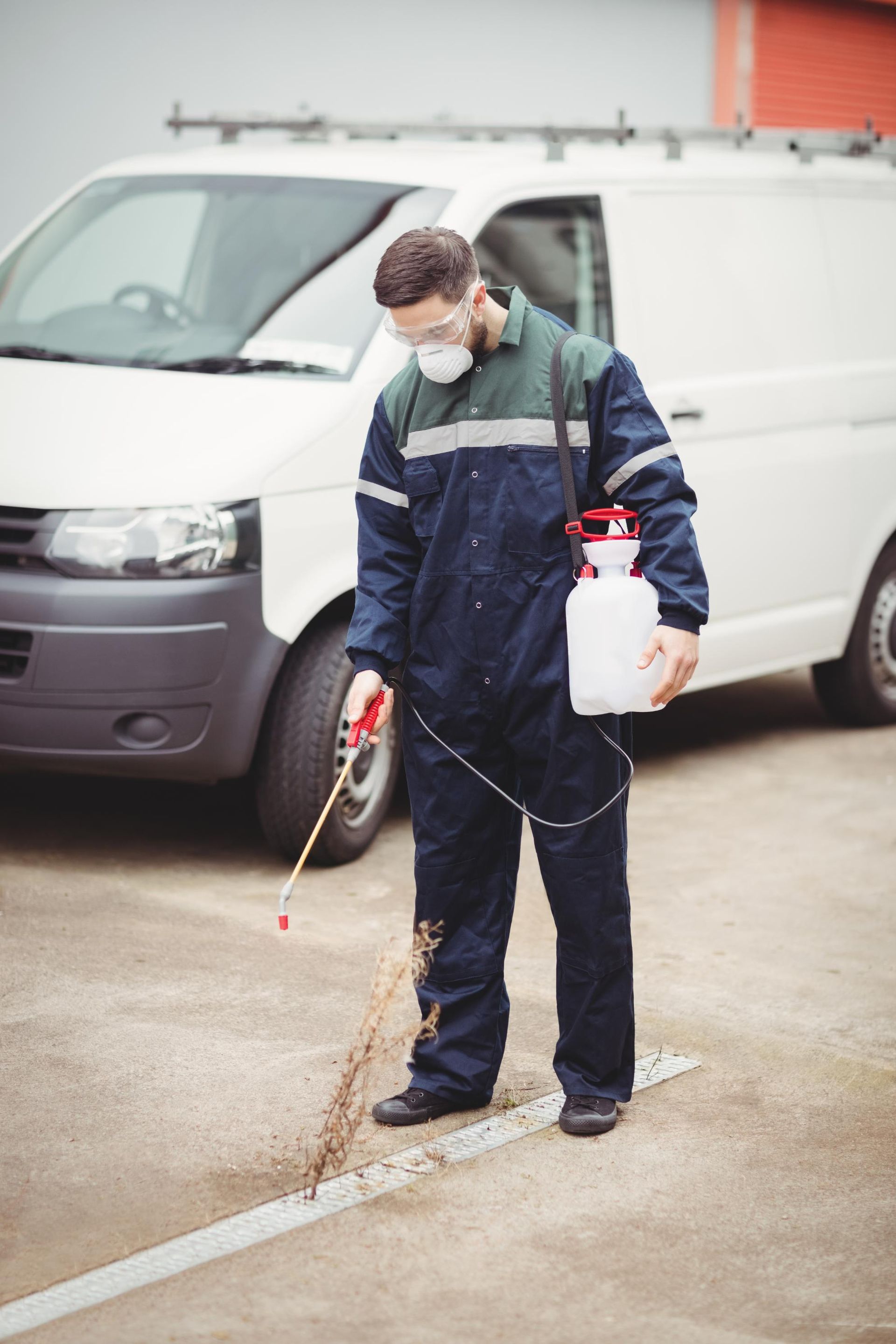 Worker in protective gear spraying pavement beside a white van