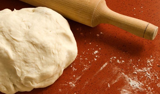 Dough ball and rolling pin on a floured red countertop, with scattered flour.