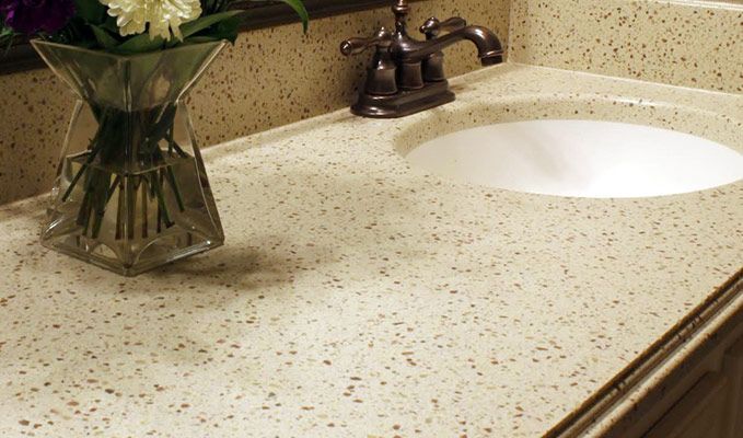 Speckled beige bathroom countertop with oval sink, bronze faucet, and a vase of flowers on the left