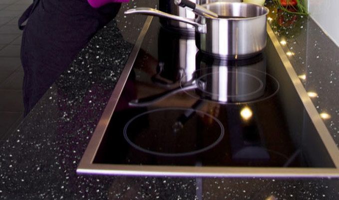 A modern black glass cooktop with a stainless steel pot on it, set into a speckled countertop.