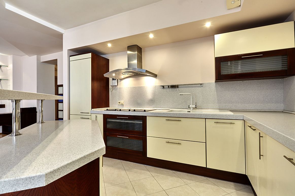 Modern kitchen with cream cabinets, dark wood accents, white countertops, and stainless steel range hood