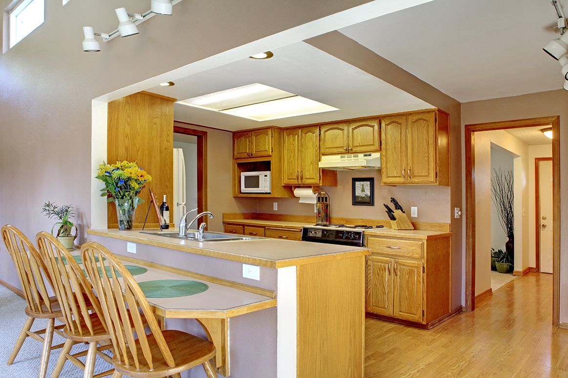 Bright kitchen with oak cabinets, white countertops, breakfast bar, and four wooden chairs in a sunlit open layout