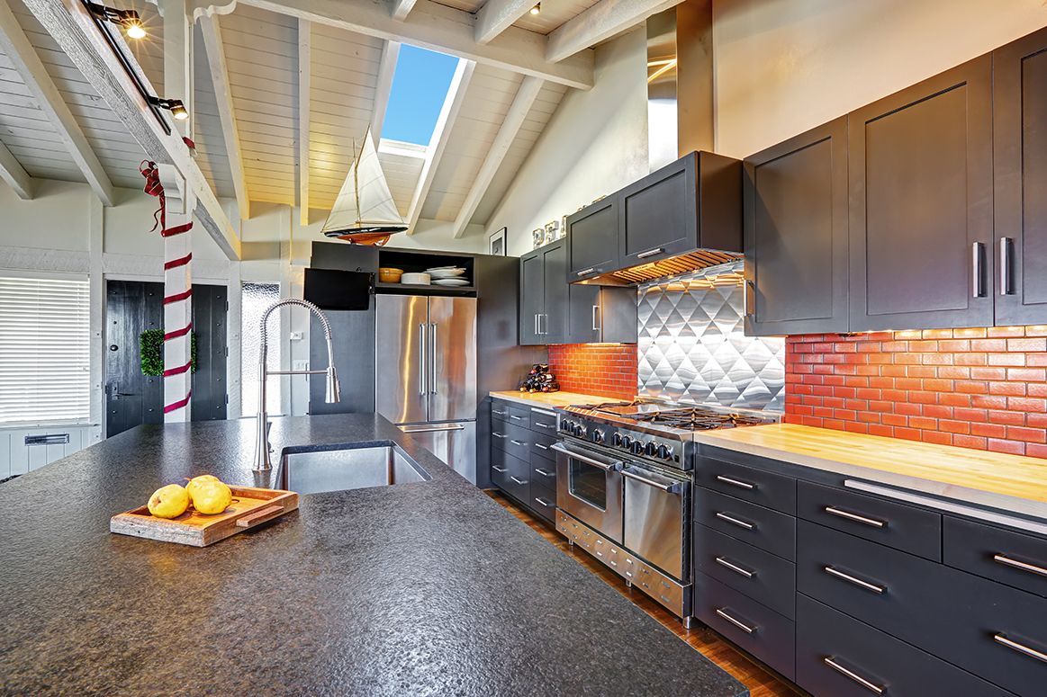 Modern kitchen with dark cabinets, granite island, stainless appliances, and red tile backsplash