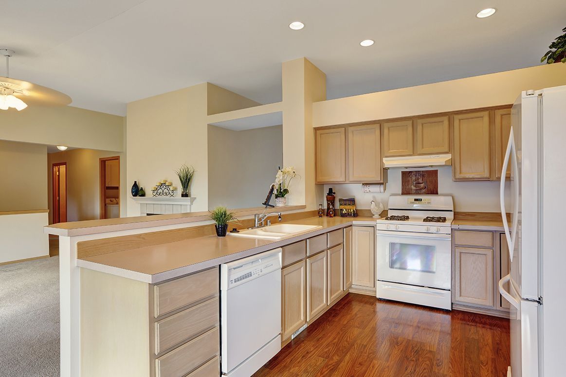 Bright kitchen with light wood cabinets, white appliances, and a breakfast bar on hardwood floors