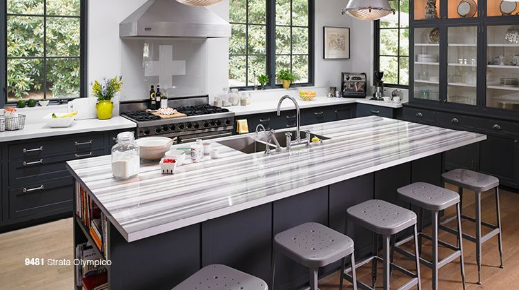 Modern kitchen with a large marble island, gray stools, stainless appliances, and black-framed windows