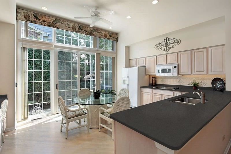 Bright kitchen with light wood cabinets, black island countertop, and glass dining table by large French doors