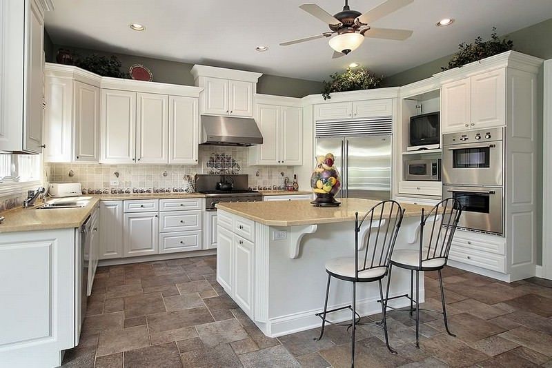 Bright white kitchen with island, stainless appliances, tiled floor, and two barstools.