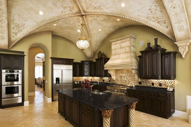 Elegant kitchen with dark wood cabinets, black granite island, arched ceiling, and stainless steel appliances